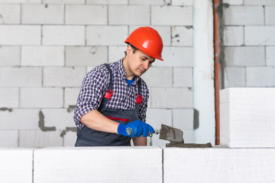 Process of bricklaying. Mason hands installing aerated concrete wall using special glue and tools necessary for brick works. Fresh mortar on aerocrete blocks. Brickwall layer with cement or glue.