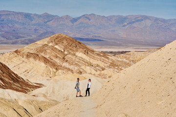 Fototapeta na wymiar A family hike from Zabriskie Point in Death Valley national park in california. Huge sand dunes, terracotta mountains and hazy horizons are shining against clear blue sky in the midday sun.
