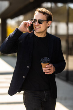 Businessman is walking to work in the city holding a coffee cup and is talking on the phone.