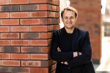 Businessman portrait on brick wall background. Young confident smiling man standing arms crossed