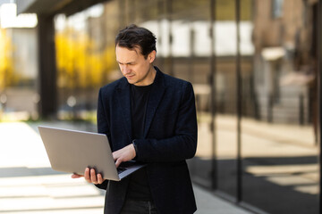 Photo of handsome young businessman walking outdoors at the street with laptop computer.