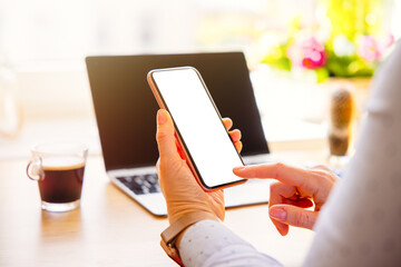 Woman working at her desk and holding mobile phone in hand with empty white screen