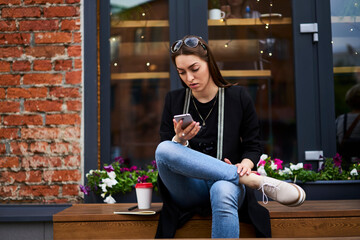 Youthful travel blogger reading browsed text on modern cellular device, millennial female student in casual clothes checking received email during online messaging on digital mobile gadget