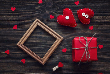 Background with blank frame, gift box and heart shapes on dark wooden table.