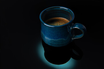 Blue handmade mug with coffee over dark background.