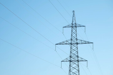 Transmission tower supporting an overhead high voltage power line on blue sky background. Power line carries wires that transport electric power from generating stations to electrical substations.