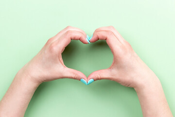 Obraz premium Female hands with mint blue nails making heart symbol on green background