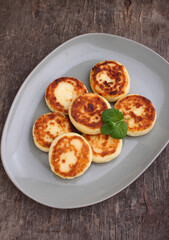 Cottage cheese pancakes or syrniki  on a plate decorated with mint, closeup view. Old wood background Russian, Ukrainian cuisine. Healthy tasty breakfast. Top view.