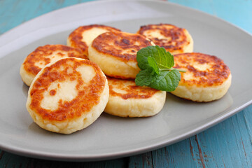 Cottage cheese pancakes or syrniki  on a plate decorated with mint, closeup view. Russian, Ukrainian cuisine. Healthy tasty breakfast. 