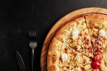 pizza on a wooden base on a black textured background top view