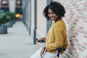 Fototapeta na wymiar Portrait of a smiling attractive black african american young woman standing over brick wall with a cool yellow urban bike