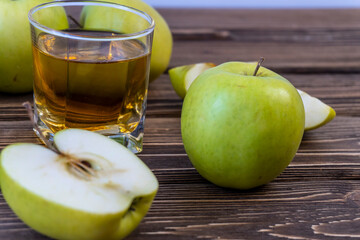 Green apples and glass with apple juice on wooden background