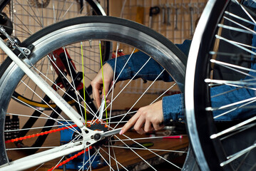 Woman in a bicycle workshop on the background of tools. Blonde in a blue denim shirt repairs a bicycle. The concept of professional bicycle service.