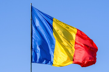 Romanian national flag blowing in the wind in direct sunlight towards clear blue sky.