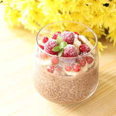 Chocolate chia seeds pudding smoothie with frozen raspberries and currants with fresh mint. Vegan, dairy-free healthy milk for breakfast with yellow flowers background. Plant-based food concept.