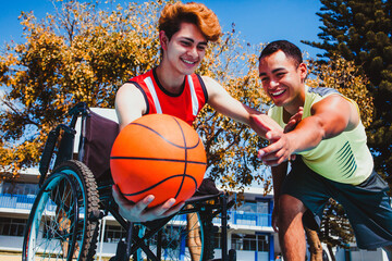 latin young man using wheelchair and playing basketball with a mexican friend in a disability...