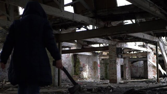 Criminal with axe stalks prey in shadows of derelict building 