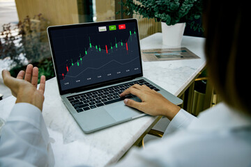 Back view of business woman sitting at desktop front laptop computer with financial graphs and statistics on screen. Successful trader and analyzing data freelance concept.