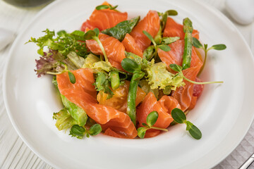 Salmon, asparagus and greens salad. On a white plate and white table.
