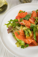 Salmon, asparagus and greens salad. On a white plate and white table.
