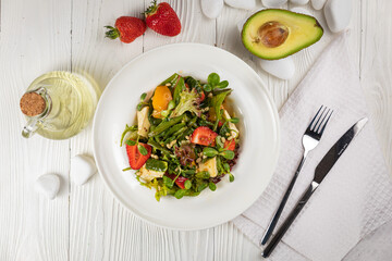Salad with strawberries, brie cheese, tomatoes and greens. On a white plate and white table.
