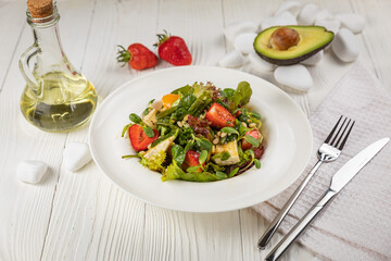 Salad with strawberries, brie cheese, tomatoes and greens. On a white plate and white table.
