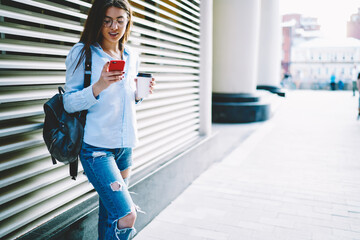 Caucasian female student in optical eyewear reading received text message using wireless connection...