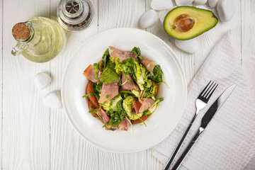 Salad with parma, mozzarella, tomatoes and greens. On a white plate and white table.
