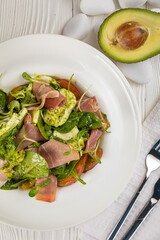 Salad with parma, mozzarella, tomatoes and greens. On a white plate and white table.

