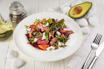 Salad of veal, goat cheese, greens. On a white plate and white table.
