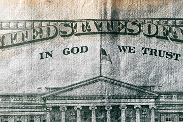 A macro close up photo emphasizing the inscription In God We Trust printed on the back of a United States ten dollar bill with selective focus on the words In God We Trust.