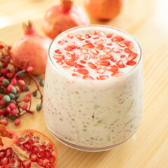 Pomegranate Punica granatum Lythraceae sarcotestas Punicoideae seeds with chia pudding. Glass closeup with red pomegranates fruit. Dairy-free cashew milk. Plant-based healthy vegan breakfast.