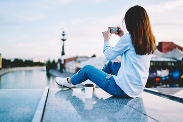 Young millennial woman using smartphone application for making photo while resting at urban...