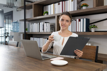 Female drinking coffee at wooden table with notebook computer in a cafe. Business woman with coffee and computer laptop working. Female drinking coffee with smiles while enjoying her leisure time.