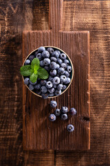Bowl of fresh blueberries on rustic wooden board. Organic food blueberries and mint leaf for healthy lifestyle.