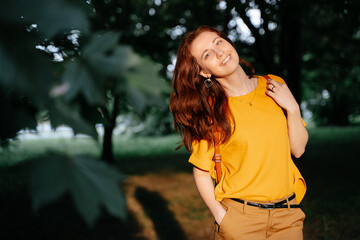 Happy young smiling girl walks in the park in the setting sun in a yellow sweater. Horizontal shot, copy space, summer time concept.