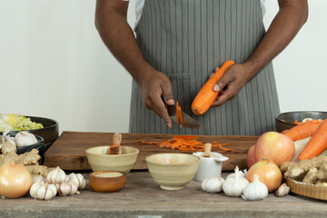 Male peeling carrot on the table. Male using knife cutting carrot on wooden table ready to cook and make kimchi.