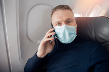 Male with safe mask passenger of airplane talking on cell phone in chair. Concept travel covid