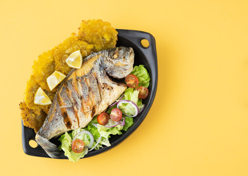 Fried fish with salad and patacones on yellow background. Copy space. Top view.