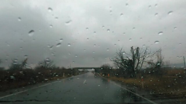 Driver POV of the windshield on the sports car with rain drops, driving on the heavy rain
