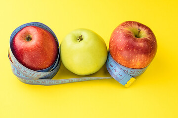 Yellow and red apples wrapped in a centimeter tape on a yellow background. Healthy food, calorie content. Fitness, diet, weight loss concept.