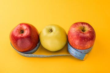 Yellow and red apples wrapped in a centimeter tape on a yellow background. Healthy food, calorie content. Fitness, diet, weight loss concept.