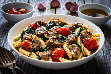 Maccheroni al ferretto with roast pork, cherry tomatoes, white mushrooms, parmesan cheese and spinach served on wooden table

