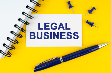 On a yellow background lies a notebook, a pen and a business card with the inscription - Legal Business