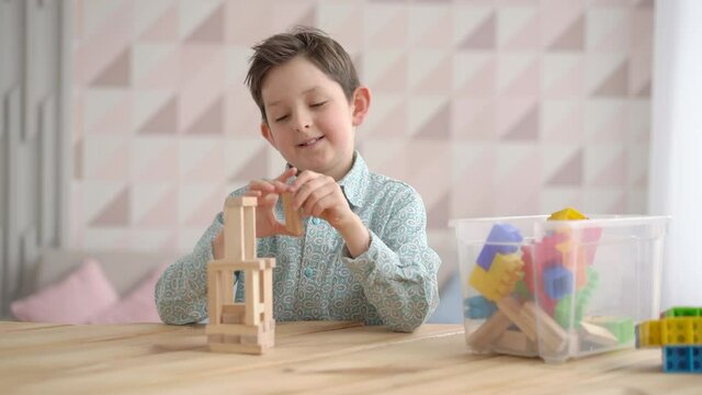 Happy cute little caucasian boy playing game building constructor tower from wooden blocks, preschooler kid having fun at home, child development, playtime concept