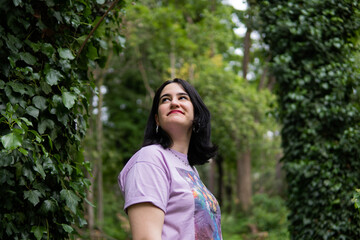 Photo of an attractive woman with black hair in the middle of nature during spring time, walking around and smiling during a sunny day