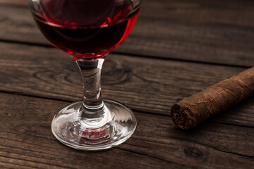 Glass of red wine and cuban cigar on an old wooden table. Close up view