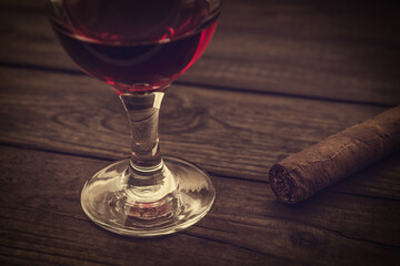 Glass of red wine and cuban cigar on an old wooden table. Close up view