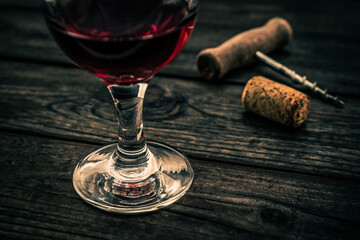 Glass of red wine and corkscrew with cork on an old wooden table. Close up view, focus on the glass of red wine