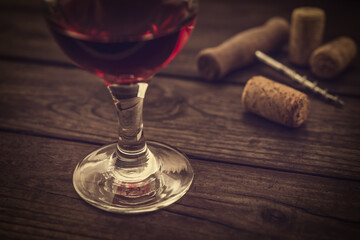 Glass of red wine and corkscrew with corks on an old wooden table. Close up view, focus on the glass of red wine